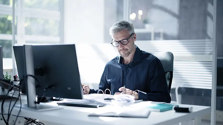 Mann sitzt an seinem Schreibtisch und überprüft Finanzdokumente im Büro, um Financial Compliance zu gewährleisten.