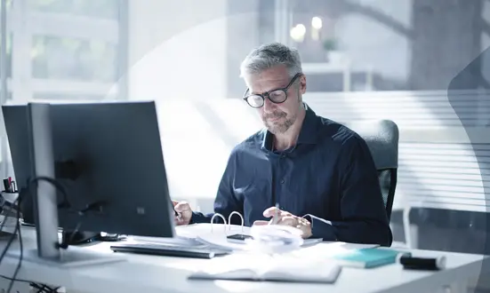 Mann sitzt an seinem Schreibtisch und überprüft Finanzdokumente im Büro, um Financial Compliance zu gewährleisten.