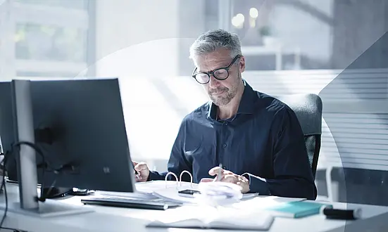 Mann sitzt an seinem Schreibtisch und überprüft Finanzdokumente im Büro, um Financial Compliance zu gewährleisten.