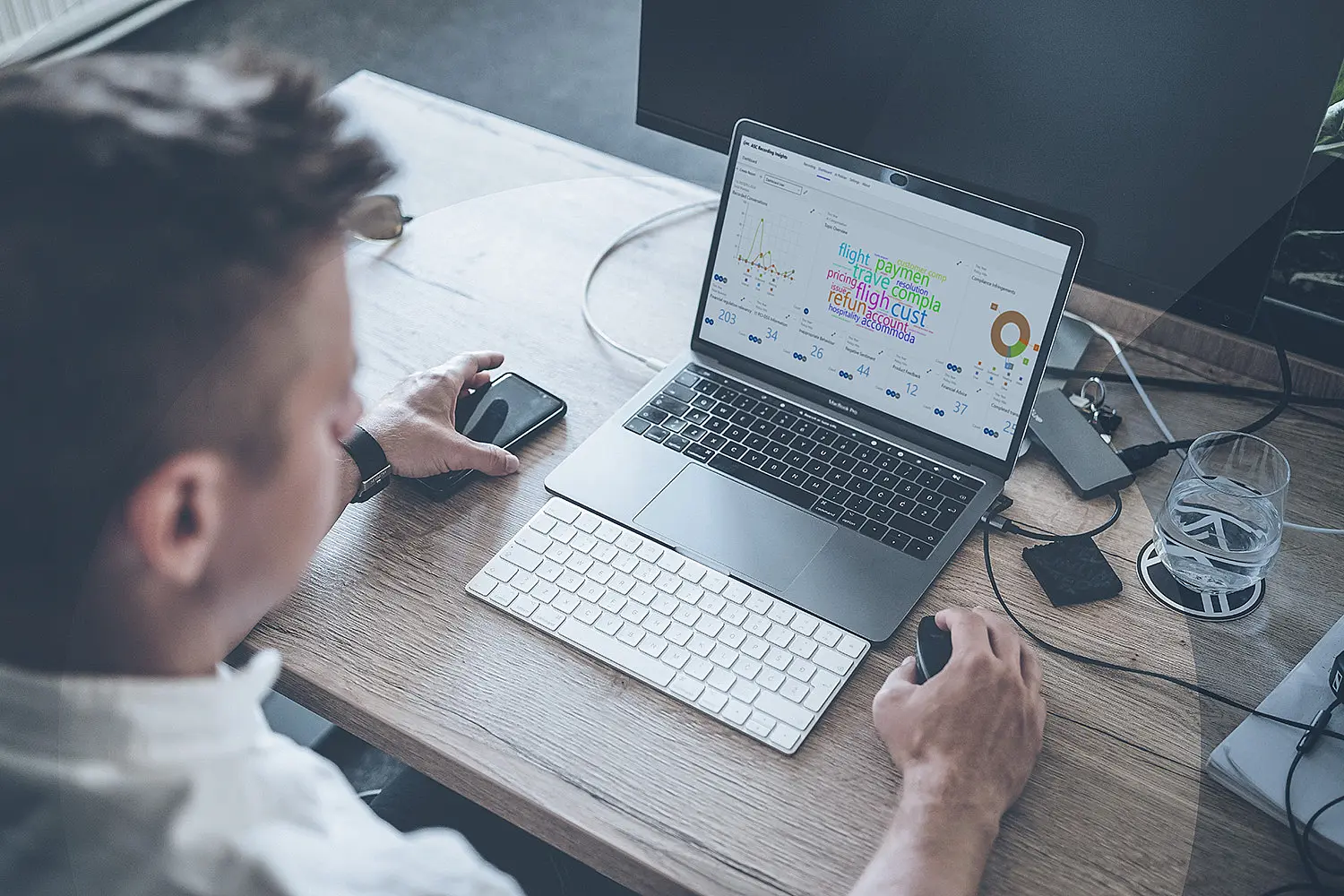 Ein Mann sitzt an einem Schreibtisch und nutzt einen Laptop, der ein Dashboard mit einer Wordcloud der ASC Recording Solution Recording Insights anzeigt.