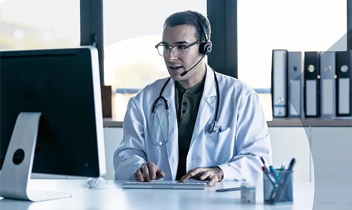 Doctor with headset in video consultation at desktop computer; illustrates modern digital patient communication