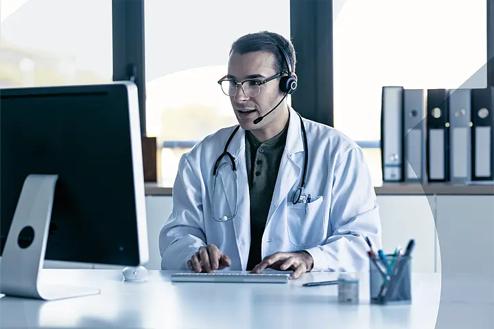 Doctor with headset in video consultation at desktop computer; illustrates modern digital patient communication